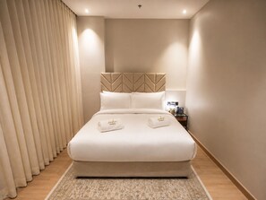 Una habitación de hotel con una cama, una mesita de noche con lámpara y una cortina.