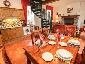 A dining area with a wooden table set for four, a kitchen with wooden cabinets, a washing machine, and a spiral staircase. - The Old Chapel, Handley (Chesterfield)