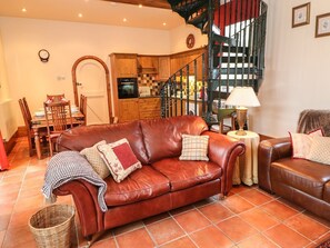 A cozy living room with a brown leather sofa, a dining table with chairs, a kitchen area, and a spiral staircase. - The Old Chapel, Handley (Chesterfield)