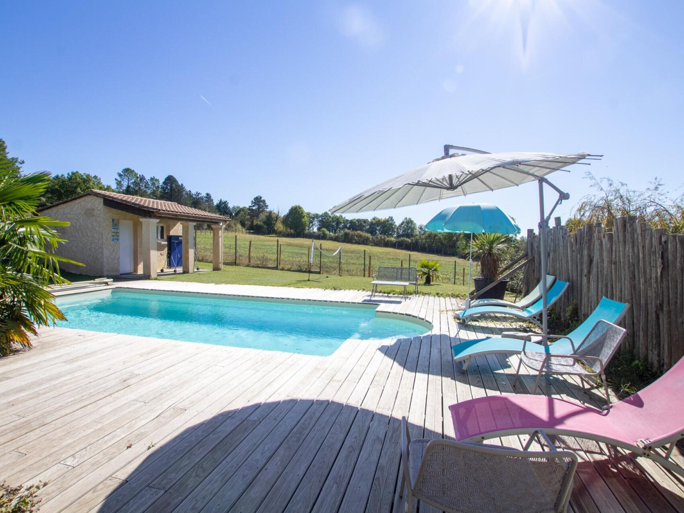 A swimming pool with a wooden deck, lounge chairs, and a covered area with umbrellas.
