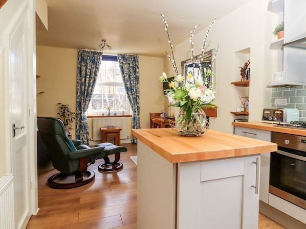 Une cuisine dotée d’un plan de travail en bois, un coin repas avec une table et des chaises, et une fenêtre avec des rideaux.