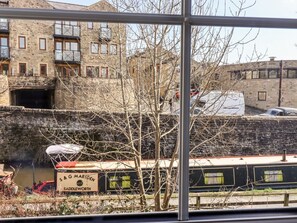 Un bâtiment historique en pierre, doté de nombreuses fenêtres et de balcons, un étroit canal navigable avec un bateau, et une vue dégagée sur le ciel.