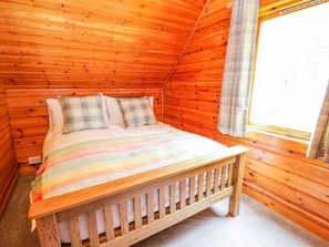Une chambre dans une cabane en bois, avec un lit, des oreillers et une fenêtre.