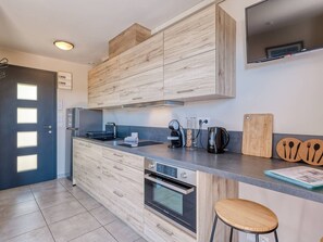 Eine moderne Küche mit Holzschränken, einem Einbauofen, einer Kaffeemaschine und einem Flachbildfernseher.