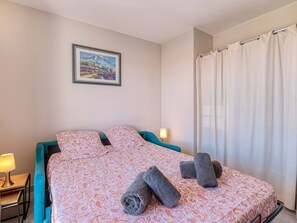 Ein Schlafzimmer mit Bett, Kissen, einer Lampe, einem Bild an der Wand und einem Vorhang.