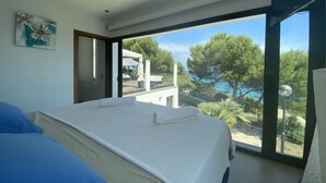 Une chambre avec un grand lit, une fenêtre donnant sur des arbres et un immeuble, et un tableau accroché au mur.