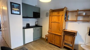 Een kleine keuken met een magnetron, spoelbak en een houten kast.