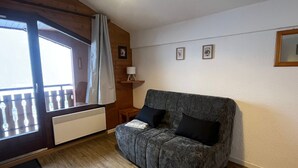 Een kamer met een grijze bank, een raam met gordijn, een radiator en lijstwerken aan de muur.