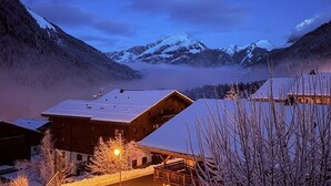 Een berglodge met een met sneeuw bedekte dak, houten gevel en uitzicht op besneeuwde bergtoppen.