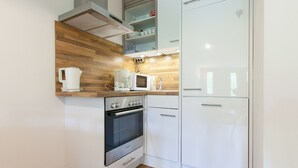 Cocina compacta con horno Bosch, armarios blancos, microondas y cafetera integrada.