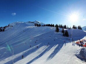 Ein verschneiter Ski-Hang mit Skifahrern, einer Seilbahn und blauem Himmel.