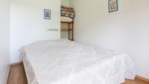 Un dormitorio con una cama, un radiador, un estante con mantas dobladas y dos cuadros en la pared.