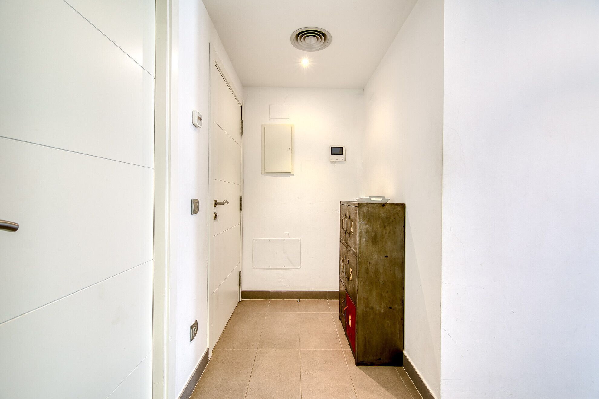 A narrow hallway with white walls, a wooden cabinet, and a ceiling light.