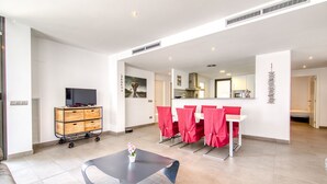 Un soggiorno moderno con un divano, un tavolo originale, un televisore su un carrello e un'area da pranzo con sedie rosse.