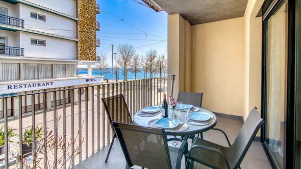 Un balcone con un tavolo apparecchiato per quattro persone, sedie, una bottiglia e bicchieri.