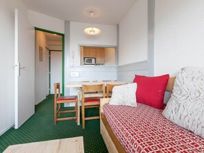 A compact room with a kitchenette, a dining area with chairs, a sofa with a patterned cover, and a green carpet. - Practical apartment with balcony - 5 guests (Avoriaz)