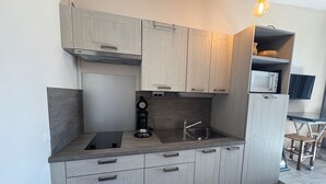 Eine moderne Küche mit grauen Schränken, einer eingebauten Mikrowelle, einer Kaffeemaschine und einer kleinen Essecke mit Tisch und Stühlen.