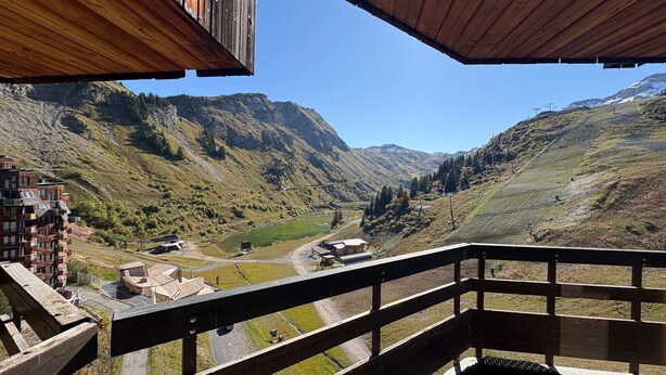 Ein Holzbalkon mit Blick auf ein gebirgiges Tal unter blauem Himmel.