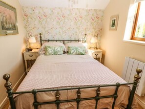 Une chambre à coucher avec un lit, deux tables de chevet, un radiateur et une fenêtre.