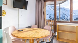 A room with a round wooden table, chairs, a TV, a window with a mountain view, and a wooden shelf. - Studio in Avoriaz, south - 4 guests (Avoriaz)