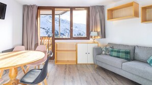 A room with a dining table, chairs, a sofa, a desk, and a window with a mountain view. - Studio in Avoriaz, south - 4 guests (Avoriaz)