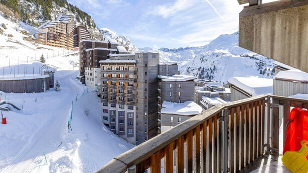 Een bergstad bedekt met sneeuw, met moderne gebouwen, een piste en een houten balkonbalustrade.