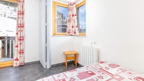 Een kamer met een bed, een klein houten krukje, een radiator en een raam met gordijnen.