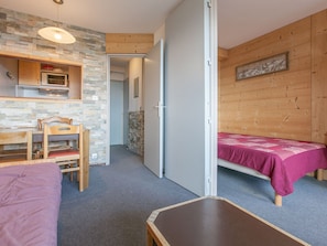 A compact room with a bed, a wooden chair, a small table, a kitchenette, and a stone wall. - Apartment for 5 guests, west-facing balcony (Avoriaz)