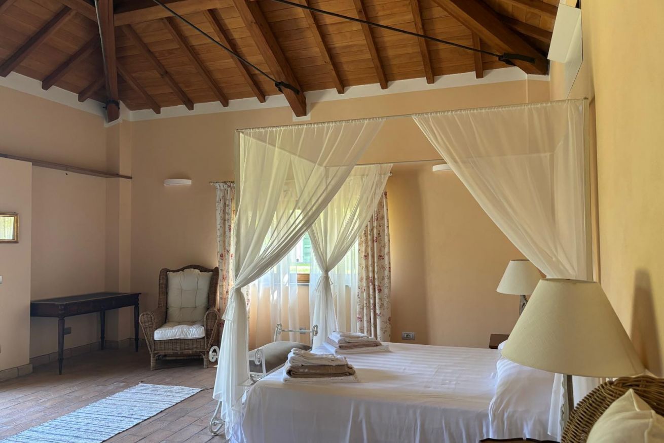 Una camera da letto con un letto a baldacchino, una sedia, un comodino e una lampada.