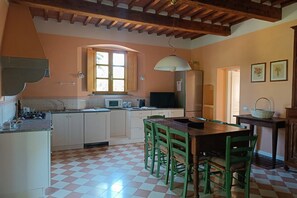 A kitchen with a checkered floor, wooden cabinets, a dining table with chairs, a hanging light fixture, and a window with a view. - Villa Aurora with Private Pool (Porto Azzurro)