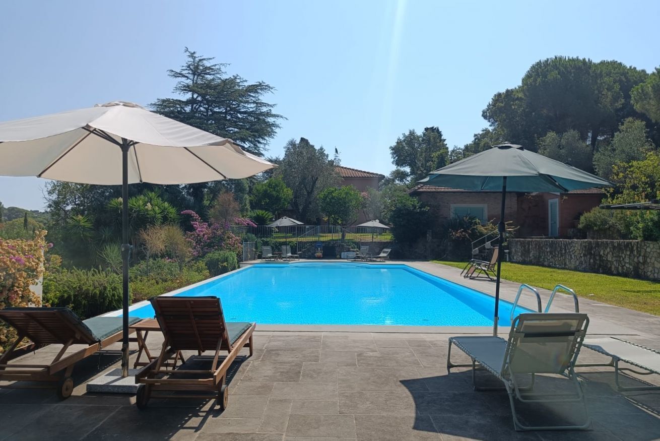 Une piscine entourée de verdure et d’une maison, avec des chaises longues et des parasols.