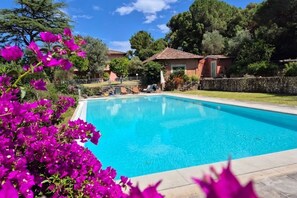 A swimming pool surrounded by a stone wall, with a clear blue sky above and lush greenery around. - Villa Aurora with Private Pool (Porto Azzurro)