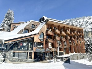 Een houten gebouw met meerdere balkons en grote ramen, omgeven door met sneeuw bedekte bomen en een helderblauwe lucht.