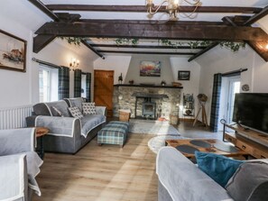 A cozy living room with a stone fireplace, wooden beams, and a television. - Ty Gwennol (977198), Llanfaethlu (Holyhead)