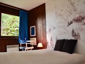 A hotel room with a bed, a desk, a chair, a window with curtains, and a wall with a mountain landscape mural. - Duplex with balcony - 6 guests (Avoriaz)