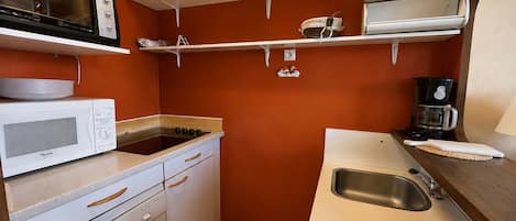 Cocina compacta con microondas, estufa, pileta y repisas superiores con utensilios de cocina.