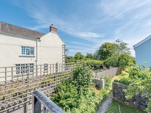 A residential property with a white exterior, a visible chimney, a fenced garden, and a stone wall. - The Hayloft, St Florence (Tenby)