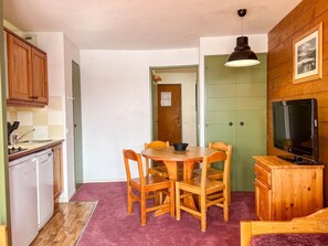 A compact kitchen with wooden cabinets, a dining table with chairs, a television, and a green door. - Peaceful studio near shops - 4 guests (Avoriaz)