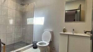 Et badeværelse med brusebad, toilet, håndvask og spejl.