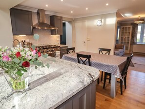 A kitchen with a granite countertop, a stove, and a dining area with a table and chairs. - 25 Maes Collen, in Llangollen. (Llangollen)