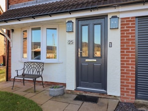 Une maison avec une porte d’entrée sombre, le numéro « 25 » au-dessus, et un banc à l’extérieur.