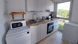 Een moderne keuken met witte kasten, een inbouwoven, een magnetron, een spoelbak en een raam met uitzicht op groen.
