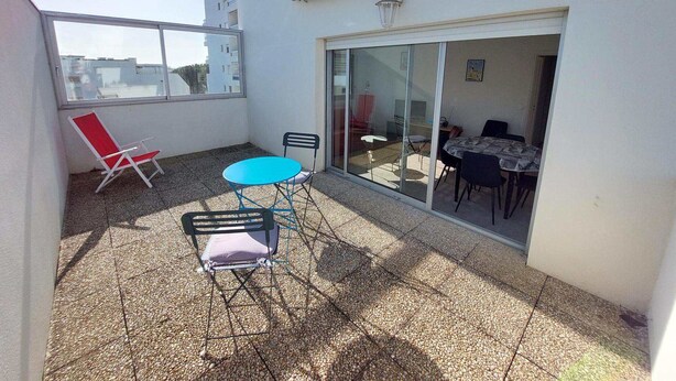 Een balkon met een tafel en stoelen, een rode stoel, en een glazen deur die leidt naar een ruimte binnen.