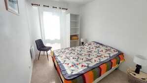 Een slaapkamer met een bed, een stoel, een bureau en een raam met gordijnen.