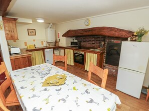 A kitchen with a wooden table, chairs, a refrigerator, a microwave, and a brick fireplace.