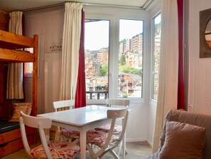 A room with a bunk bed, a table with chairs, and a view of a cityscape through a window. - Studio for 3 guests near children (Avoriaz)