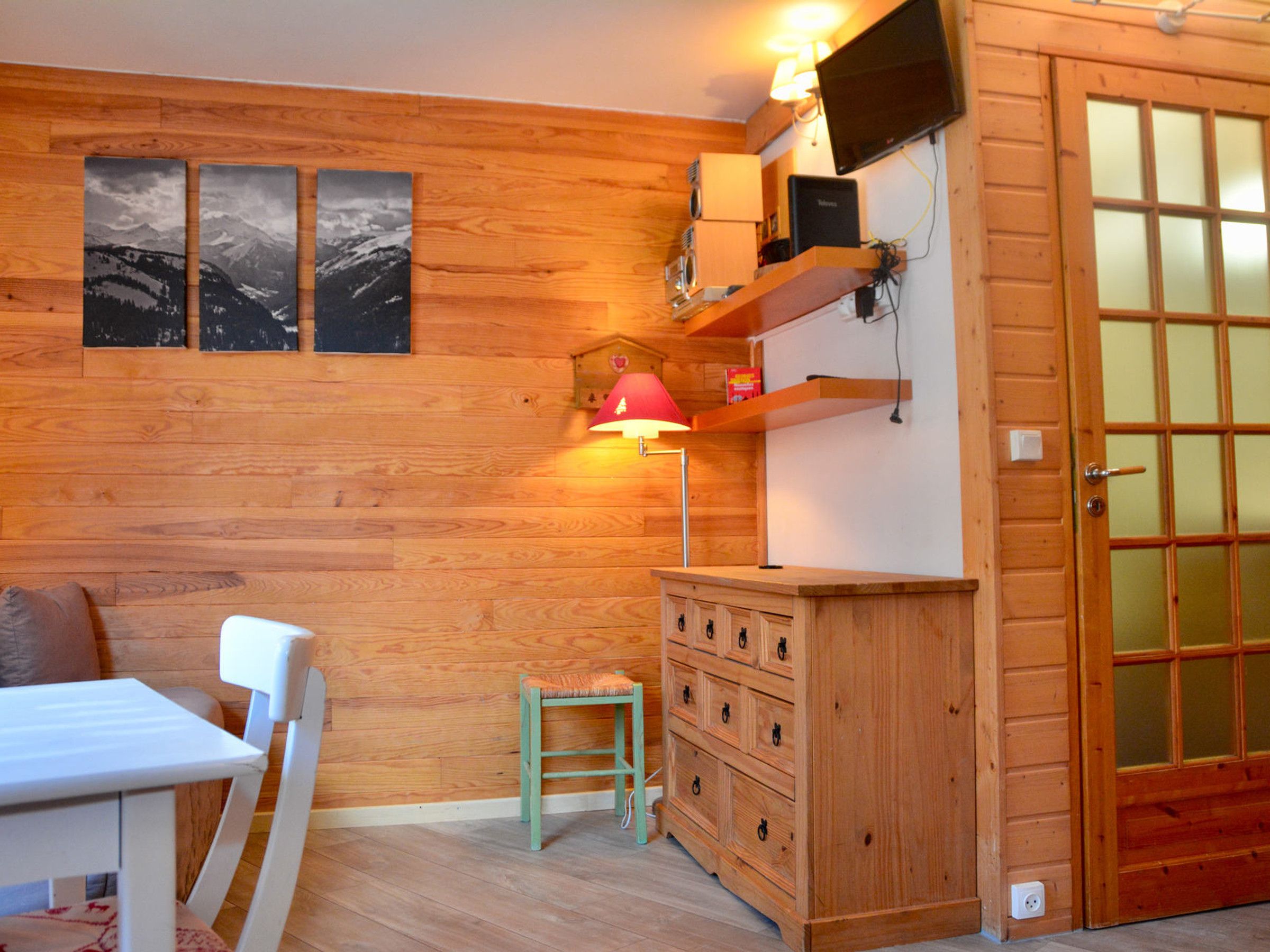 Ein Zimmer mit Holzwänden, einem weißen Tisch, einer roten Lampe und einem Holzkabinett.