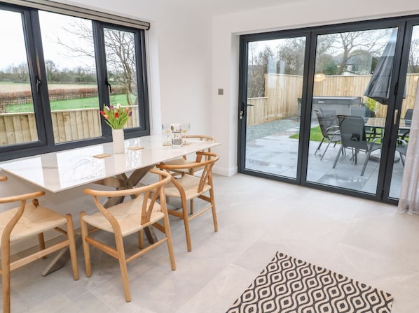 A dining area with a table and chairs, a vase with flowers, and a view through a sliding glass door to an outdoor patio.