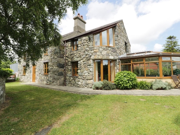 A stone house with a large glass window, a chimney, and a well-maintained lawn.