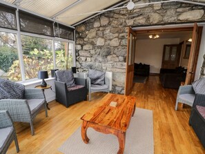 A room with wicker furniture, a wooden coffee table, stone walls, and large windows.